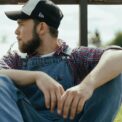 man in blue denim vest and black cap sitting on brown wooden chair