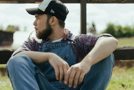 man in blue denim vest and black cap sitting on brown wooden chair