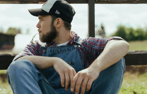 man in blue denim vest and black cap sitting on brown wooden chair